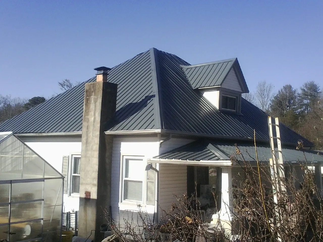 Dark blue standing seam metal roof on a white farmhouse with dormer — Slate & Tile Roof Repair by Roofing Brothers in Saint Stephen