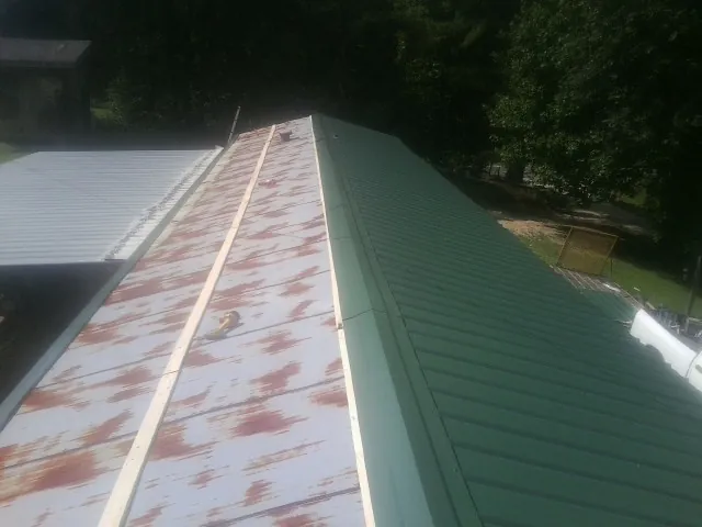Old rusted panels beside newly installed green metal roofing — Wind Damage Roof Repair by Roofing Brothers in Saint Stephen