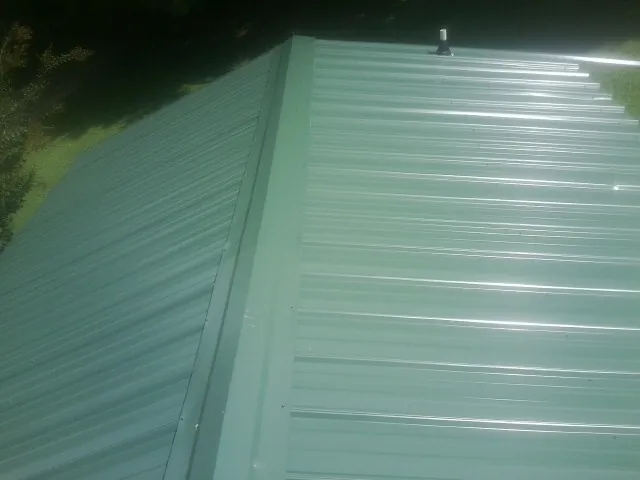 New green metal panels meeting at the ridge of a roof — Flat Roof Repair work by our crew in Saint Stephen