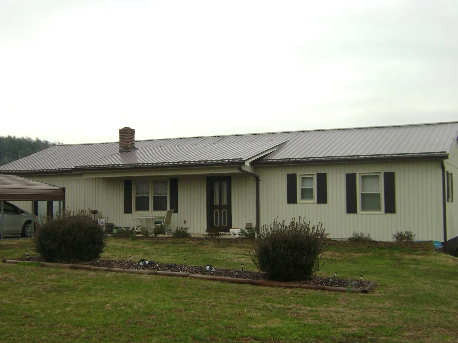 Brown metal roof on a cream sided ranch home with a brick chimney in Saint Stephen