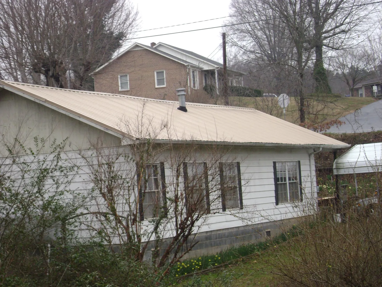 Tan metal roof on a white sided house set into a hillside — Commercial Roofing by Roofing Brothers in Saint Stephen